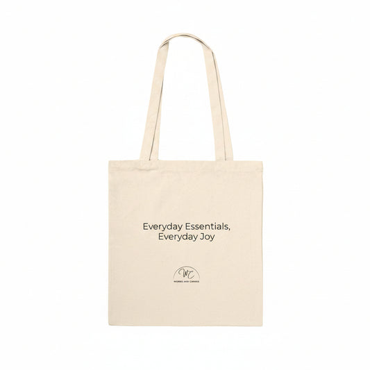 A natural beige canvas tote bag with black printed text reading 'Everyday Essentials, Everyday Joy' and a small circular logo below, shown on a plain white background.