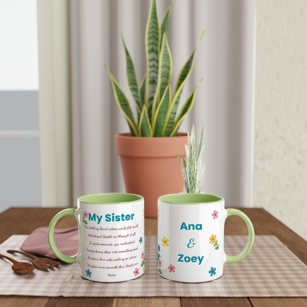 Two white ceramic mugs with light green interiors and handles are displayed on a wooden table in a styled indoor setting. One mug shows the text 'My Sister' with a poem, and the other shows 'Ana & Zoey' with small colorful flowers.