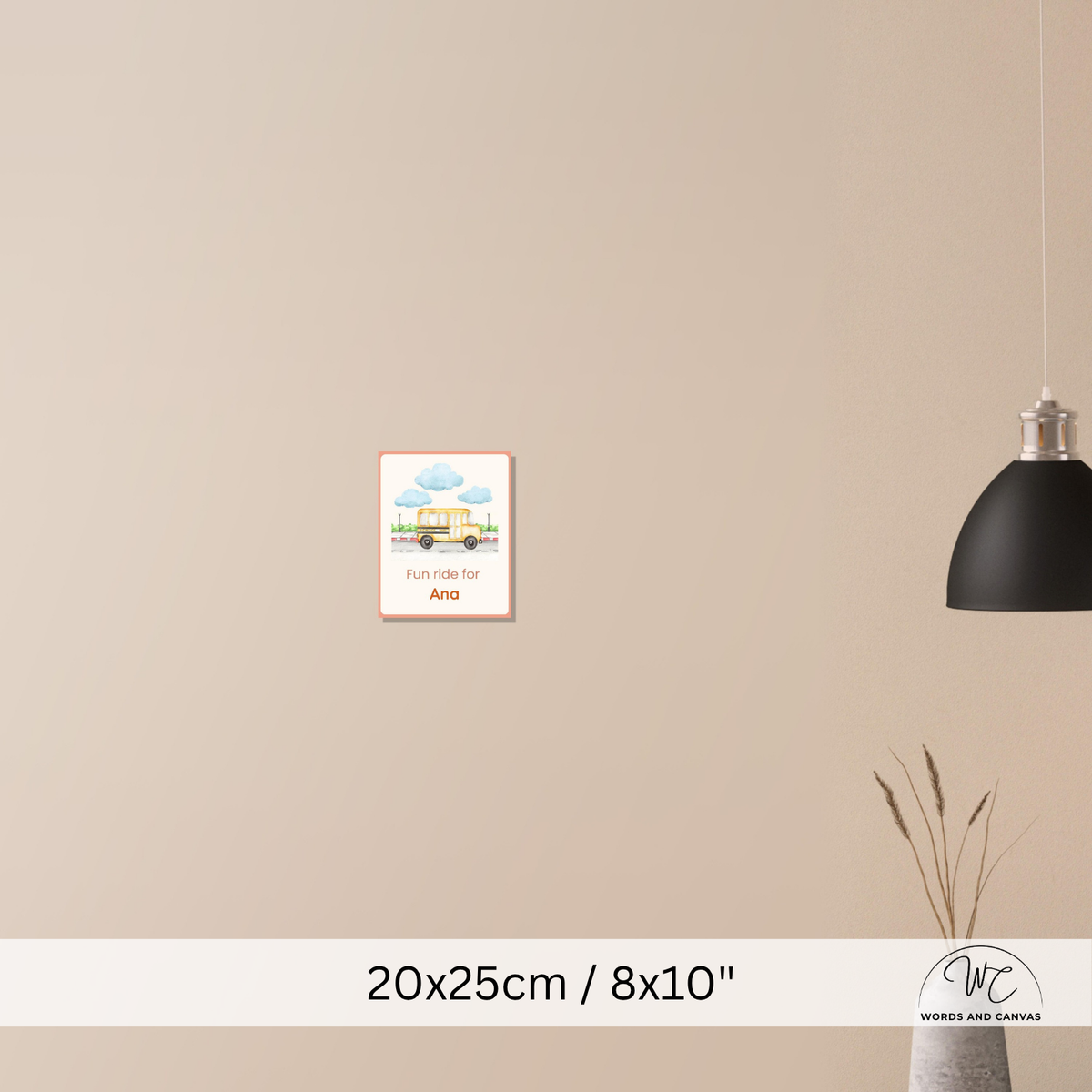 A small framed wall art print hangs on a beige wall in a styled interior. The print shows a colourful illustration of a house under blue clouds with the text 'Fun ride for Ana'.