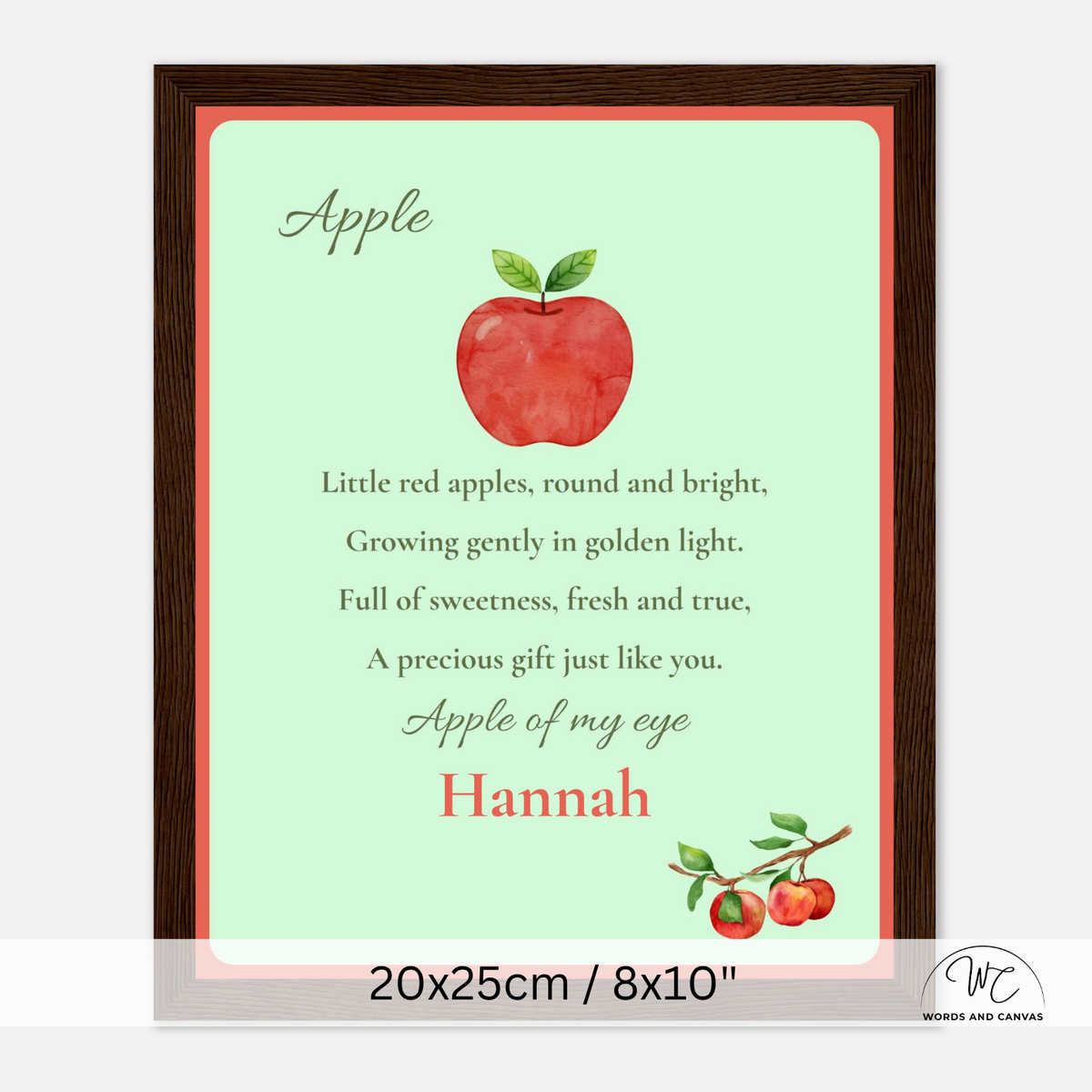 A personalized dark wooden framed apple-themed nursery print with a watercolor red apple, poem text, and the name Hannah, shown in a dark wood frame on a light gray background.