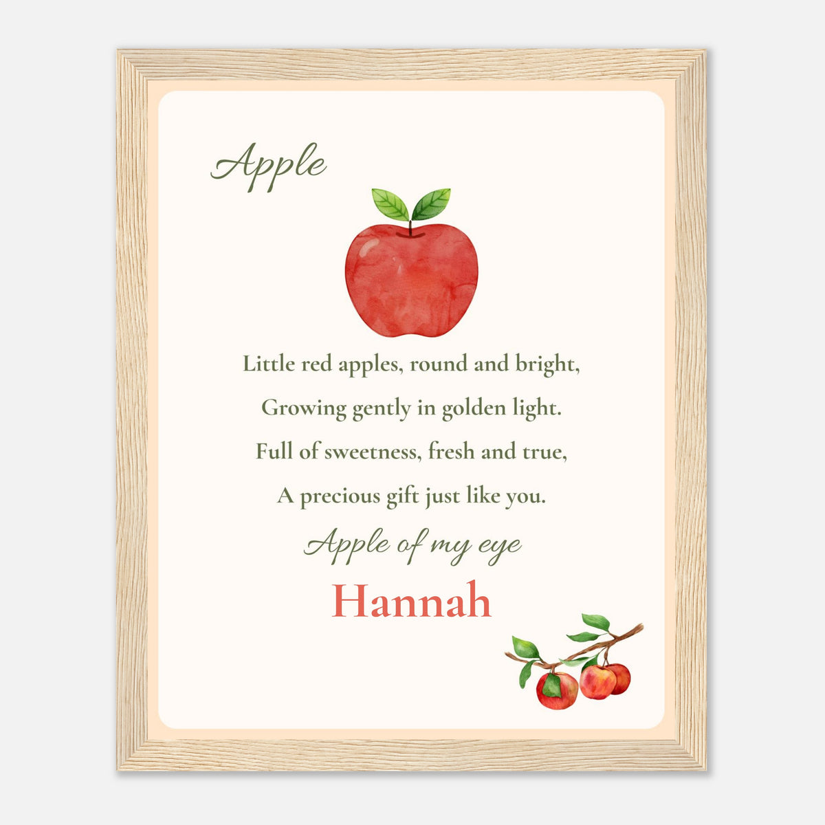 A framed personalized nursery print featuring a watercolor red apple with green leaves and the nursery rhyme 'Apple of my eye' with the name 'Hannah' in red script, set in a light wood frame.