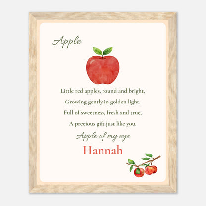 A framed personalized nursery print featuring a watercolor red apple with green leaves and the nursery rhyme 'Apple of my eye' with the name 'Hannah' in red script, set in a light wood frame.
