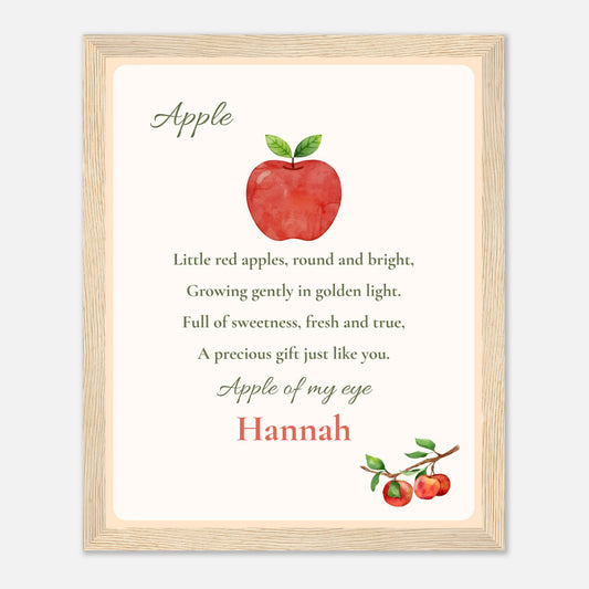 A framed personalized nursery print featuring a watercolor red apple with green leaves and the nursery rhyme 'Apple of my eye' with the name 'Hannah' in red script, set in a light wood frame.