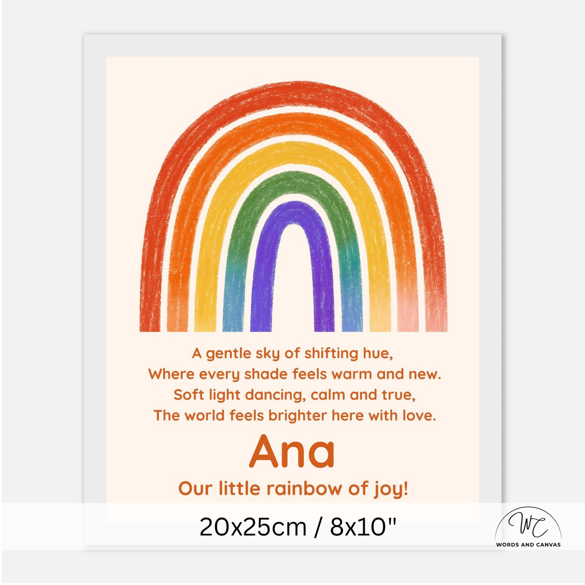 A personalized children's nursery art print featuring a colorful rainbow and a poem. The print has a cream background, a vibrant rainbow with orange, red, yellow, green, blue, and purple bands, and the name 'Ana' along with the phrase 'Our little rainbow of joy!' printed in orange.