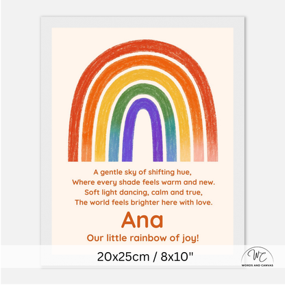 A personalized children's nursery art print featuring a colorful rainbow and a poem. The print has a cream background, a vibrant rainbow with orange, red, yellow, green, blue, and purple bands, and the name 'Ana' along with the phrase 'Our little rainbow of joy!' printed in orange.
