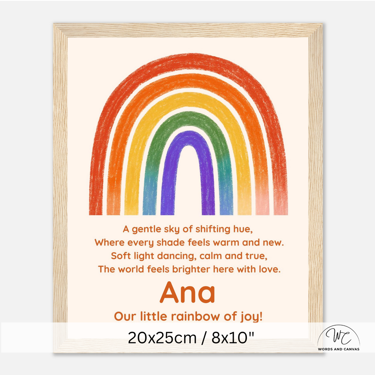 Personalized framed children's art print featuring a colorful rainbow and a poem, with the name 'Ana' and the text 'Our little rainbow of joy!' shown on a light wood frame against a white background.