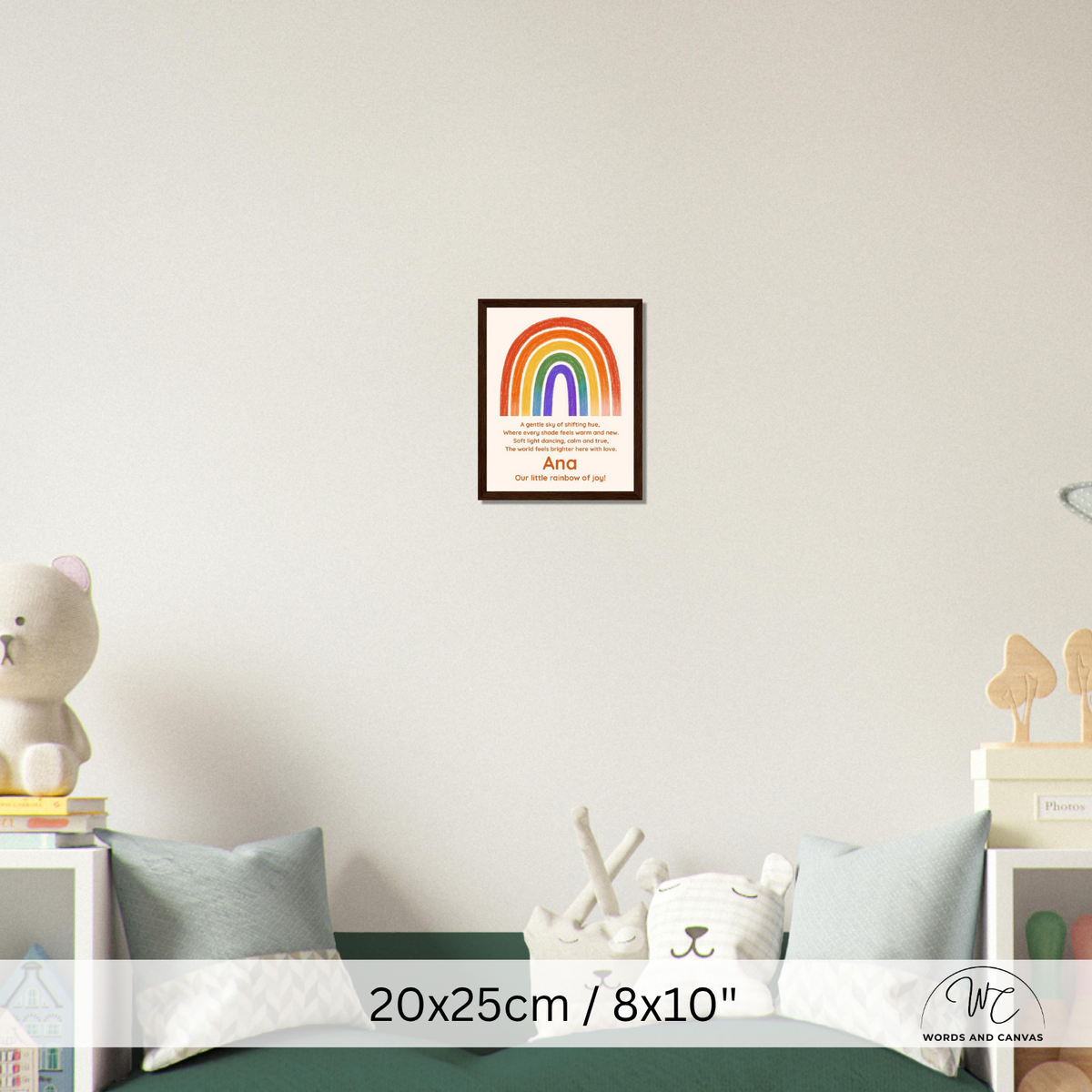 A framed personalized children's nursery art print featuring a colorful rainbow and the name 'And' on a warm cream background, displayed on a light gray wall above a green bed in a styled bedroom setting.