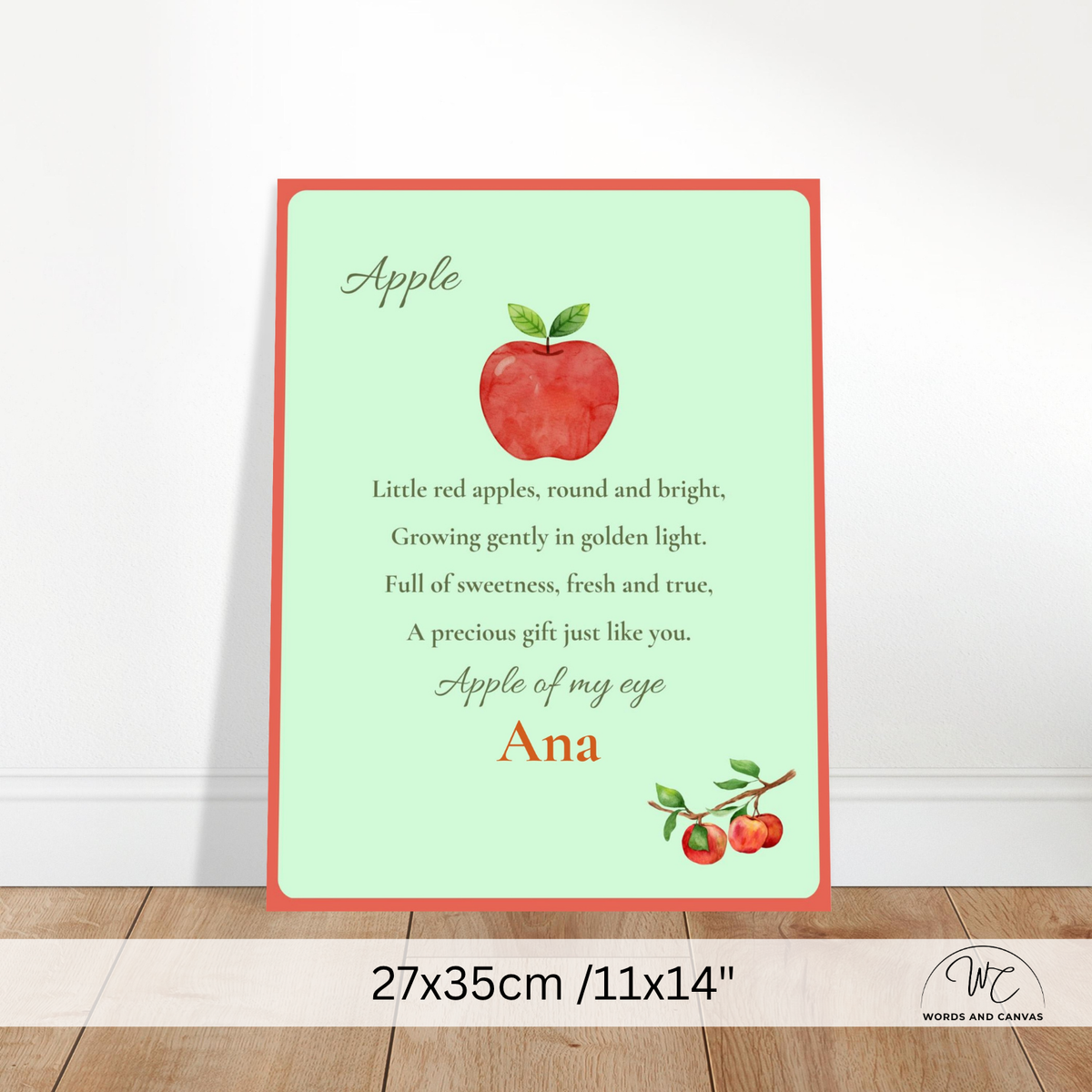 A personalized apple-themed nursery print with a red border, a watercolor red apple, and a poem printed on a mint green background, shown leaning against a white wall on a wooden floor. A size label at the bottom reads 27x35cm / 11x14".