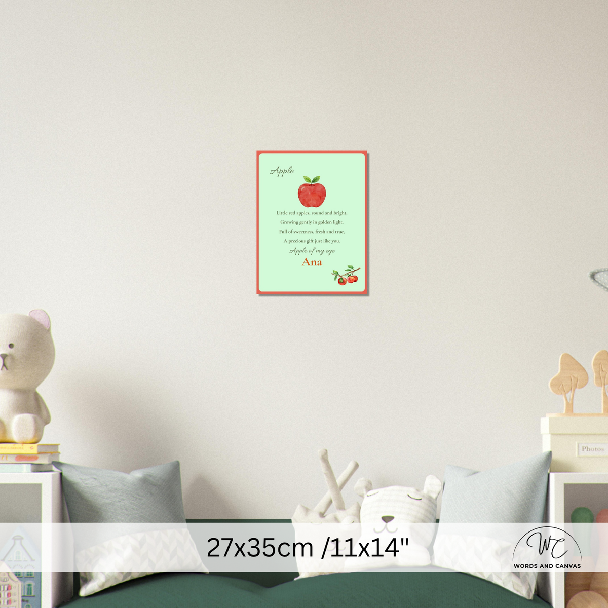 A personalized children's apple poster displayed on a nursery wall above a bed. The poster features a light green background with a red border, an illustration of a red apple, poem and a custom name, 'Ana'.
