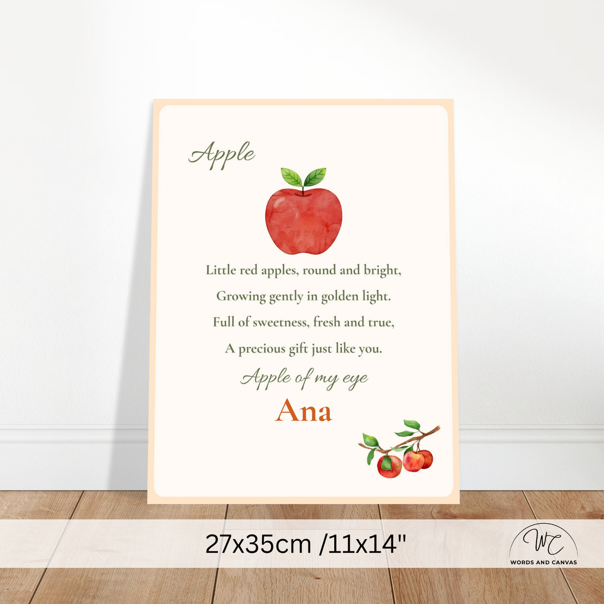 A personalized children's wall print featuring a red apple illustration and a poem about apples, with the customizable text 'Apple of my eye' and 'Ana' in orange. The print is displayed leaning against a white wall on a wooden floor, with a size overlay at the bottom indicating 27x35cm / 11x14 inches.