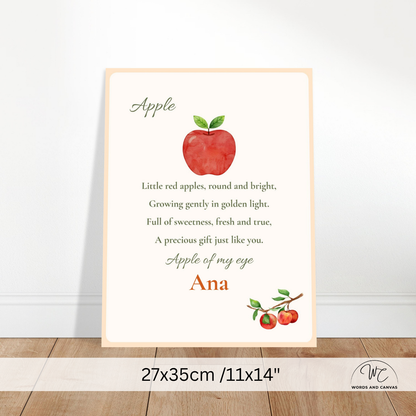 A personalized children's wall print featuring a red apple illustration and a poem about apples, with the customizable text 'Apple of my eye' and 'Ana' in orange. The print is displayed leaning against a white wall on a wooden floor, with a size overlay at the bottom indicating 27x35cm / 11x14 inches.