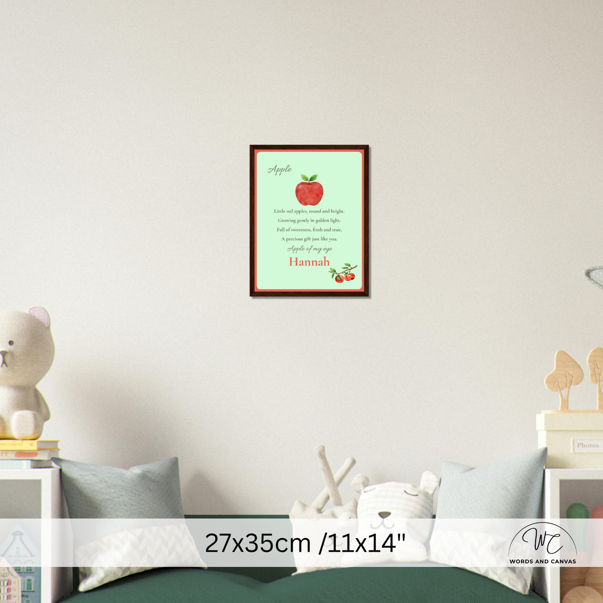 A framed personalized apple-themed nursery print hangs on a white wall above a bed. The print features a red apple, the name 'Hannah', and a poem.