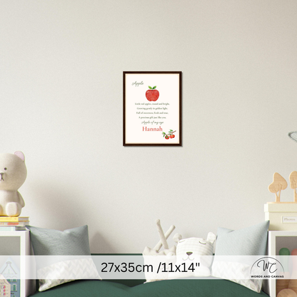 A framed personalized apple-themed nursery wall art print hangs on a light gray wall above a bed. The print features a red apple, the word 'Apple,' a short poem, and the name 'Hannah' in red at the bottom.