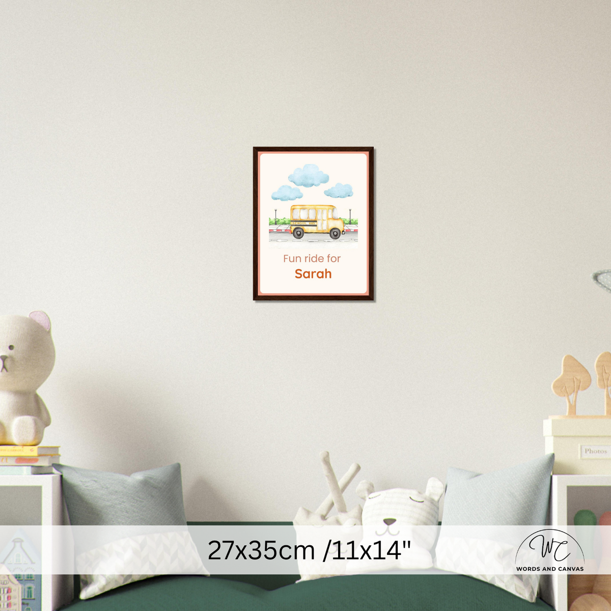 A framed children's wall art print hangs on a light gray wall above a bed. The print shows a yellow school bus with blue clouds and the text 'Fun ride for Sarah.