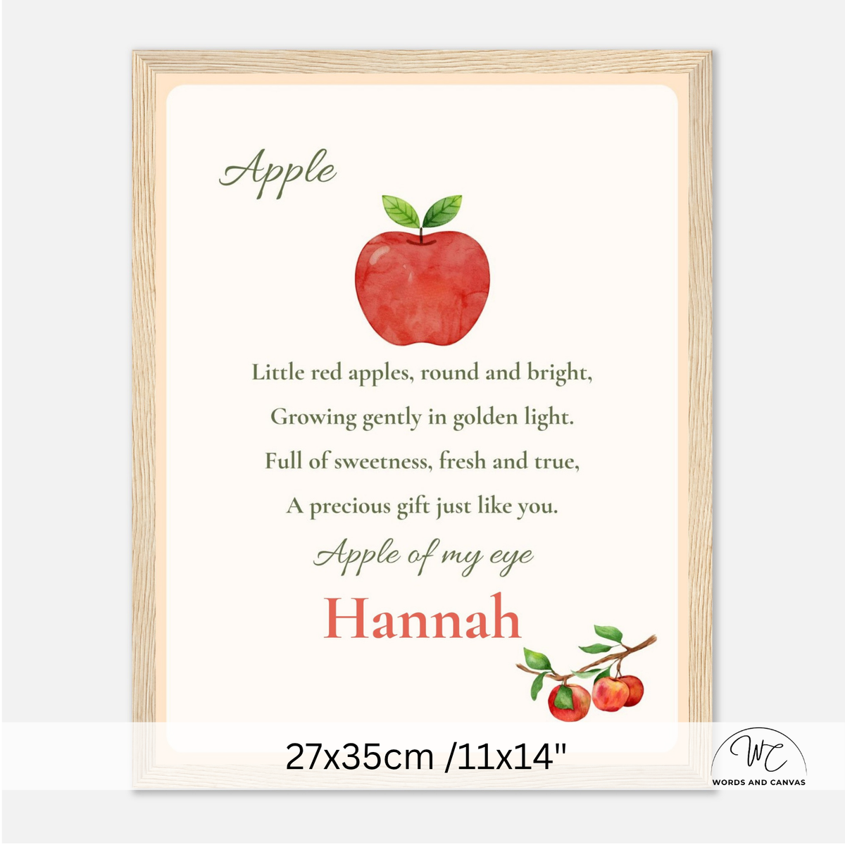 A framed personalized nursery art print featuring a watercolor red apple with green leaves and nursery rhymes. The text reads 'Apple' and 'Apple of my eye' with the name 'Hannah' in red. 27x35cm size.