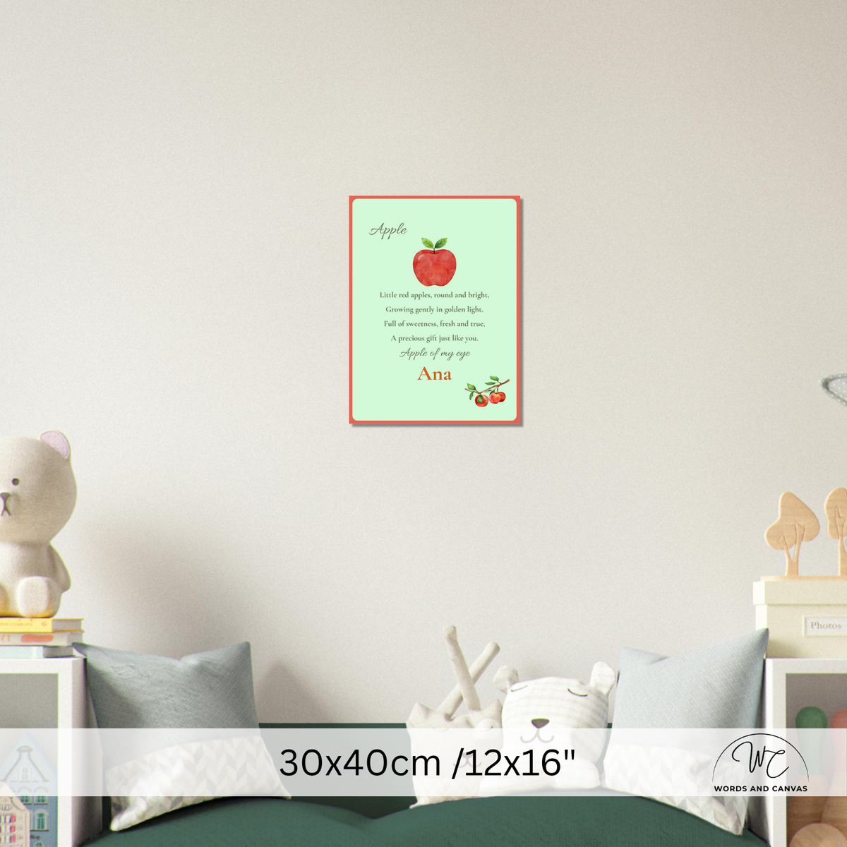A personalized apple-themed nursery wall art print displayed on a light grey wall above a bed. The print features a light green background with a red border, a red apple illustration, and the name 'Ana' 