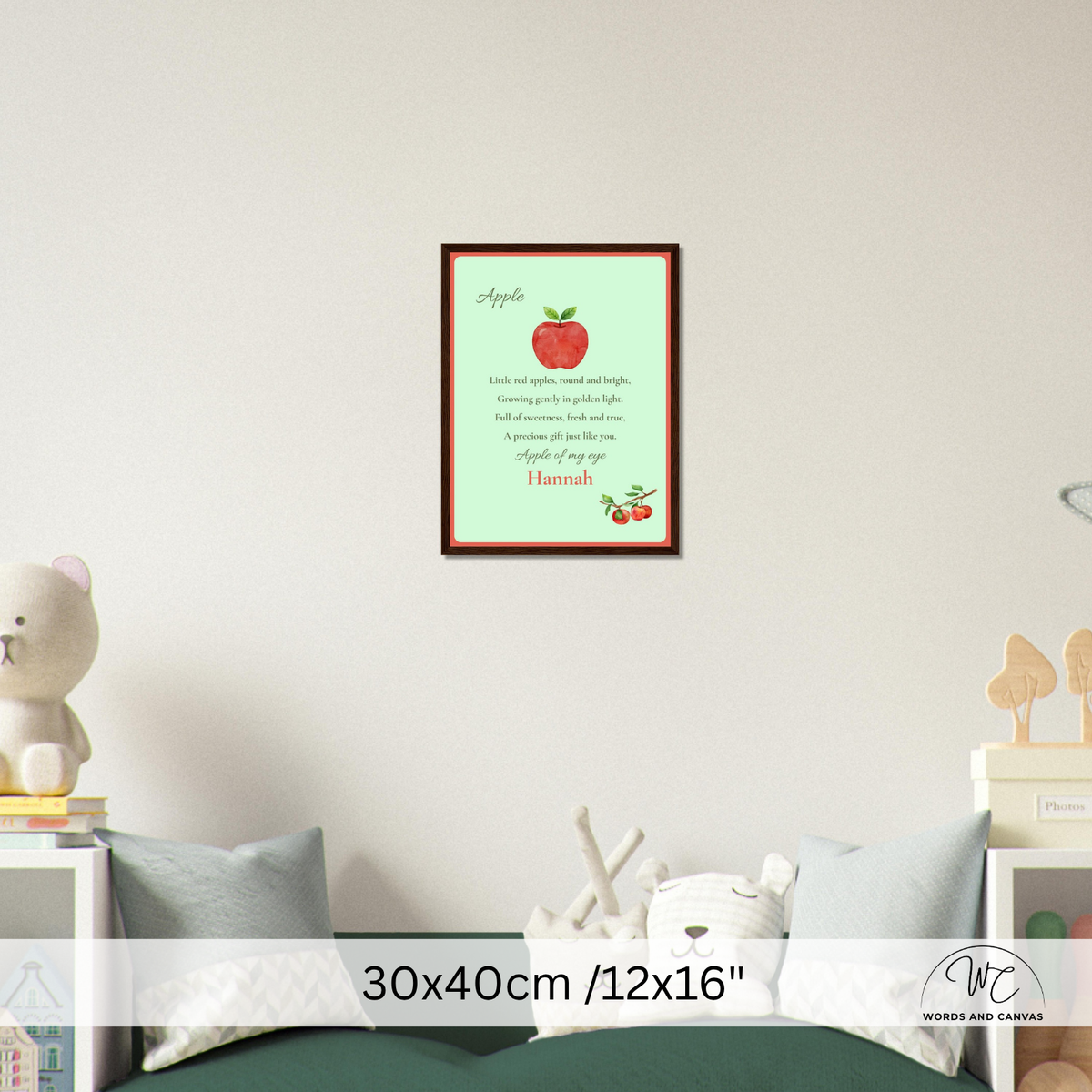 A framed personalized apple-themed nursery print hanging on a light gray wall above a bed. The print features a red apple, a poem about apples, and the name 'Hannah' 
