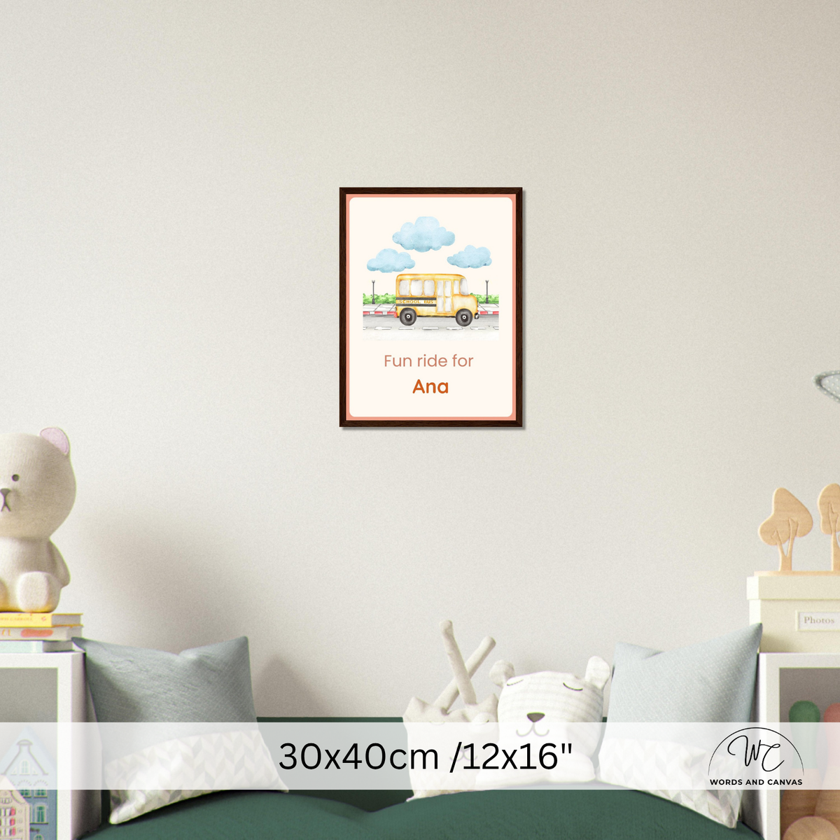A framed personalized children's wall art print hangs on a light gray wall above a bed. The print shows a yellow school bus under blue clouds with the text 'Fun ride for Ana'.