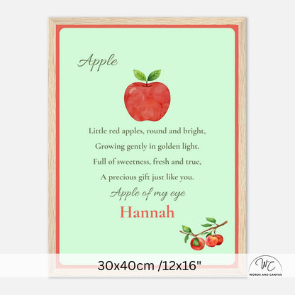 A personalized framed apple-themed nursery print with a light green background, red apple illustration, and the text 'Apple of my eye Hannah' in coral and dark green. The print is shown in a light wood frame against a white background, with a size label at the bottom reading 30x40cm /12x16".