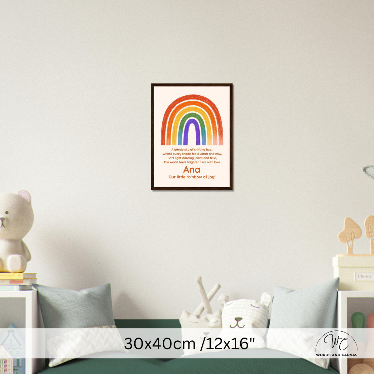 A framed personalized rainbow children's nursery wall art print hanging on a light gray wall above a green bed. The poster features a colorful rainbow arch with the text 'And our little rainbow of joy!'.