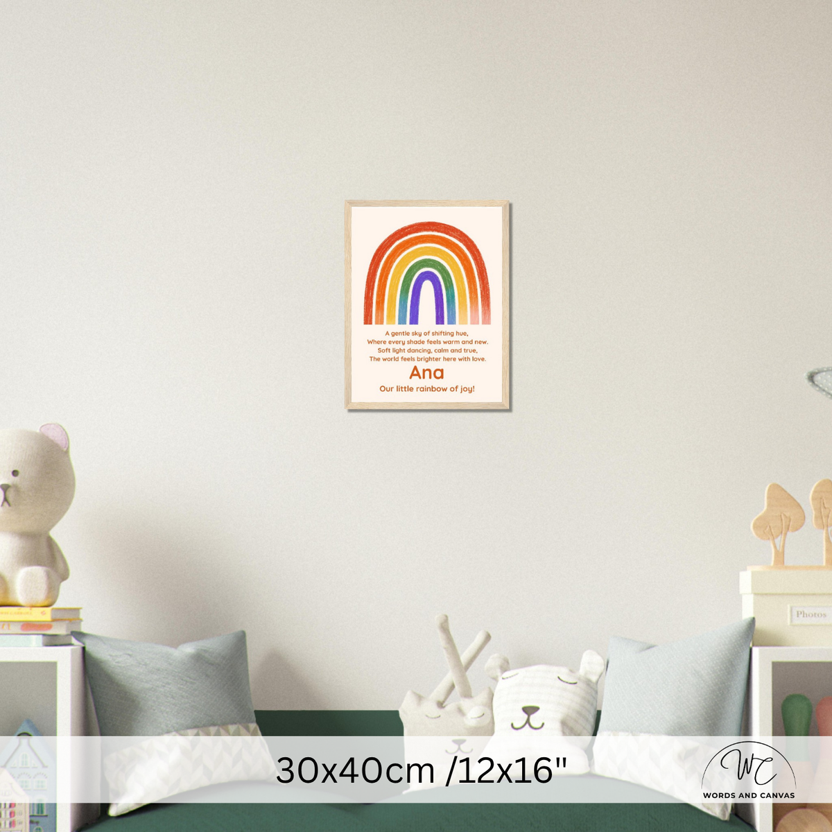 A framed personalized children's nursery art print featuring a colorful rainbow and the text 'Our little rainbow of joy' with the name 'Ana', displayed on a light gray wall above a bed in a styled nursery setting.