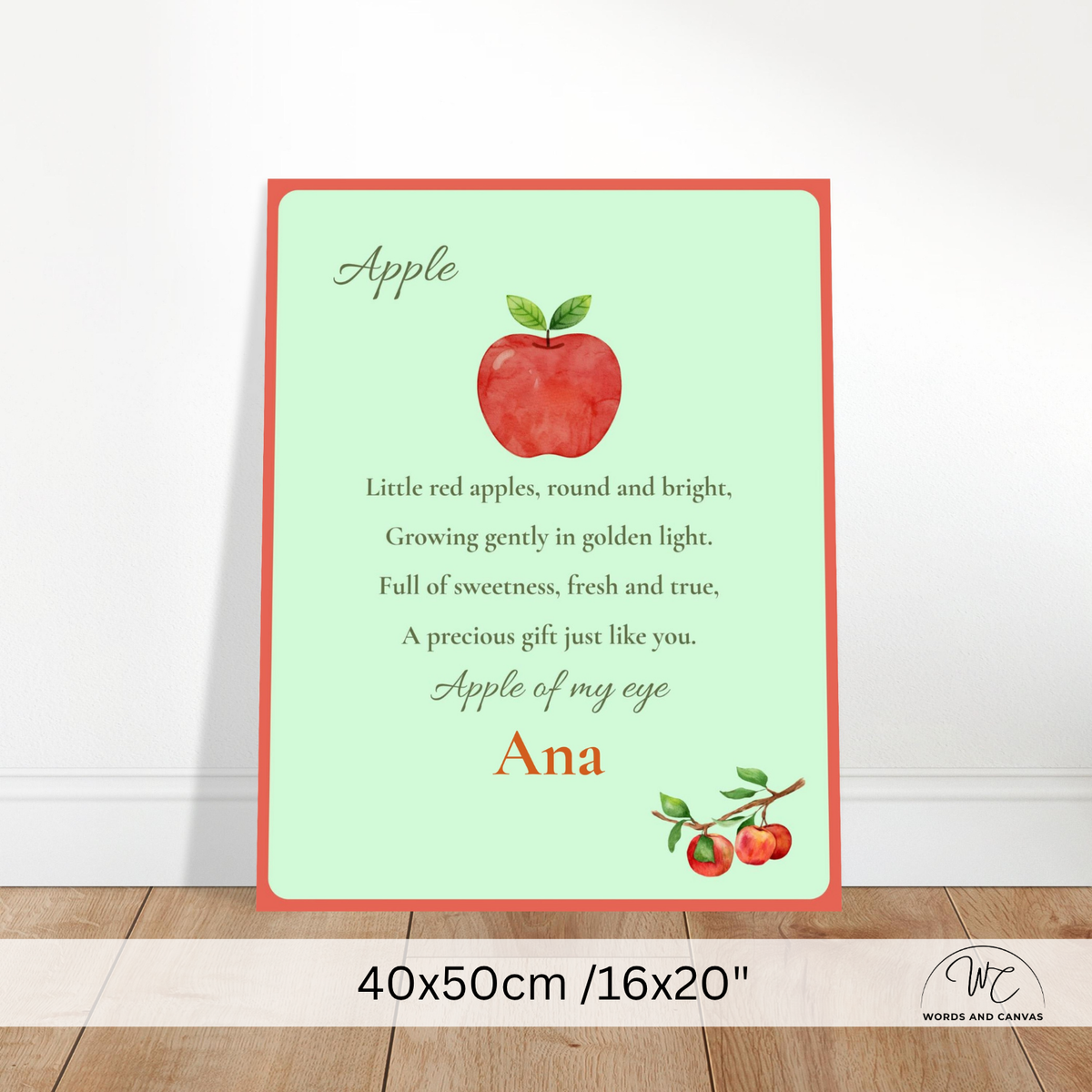 Personalized apple-themed nursery wall art print with a red border, a watercolor red apple, and a poem, shown leaning against a white wall on a wood floor. The bottom has a size label reading 40x50cm /16"x20" and a Words and Canvas logo.