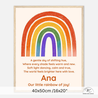 A framed personalized children's art print featuring a colorful rainbow and a poem. The print has a cream background, a light natural wood frame, and the name 'Ana' printed in orange above the phrase 'Our little rainbow of joy!'.