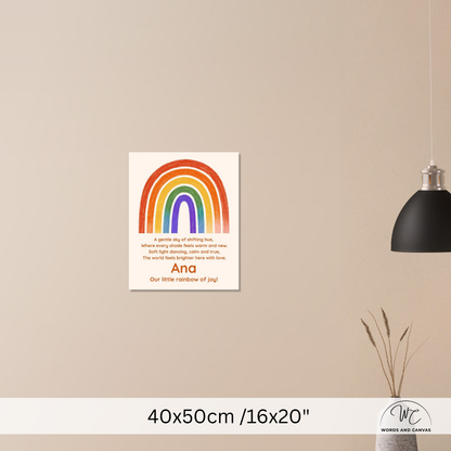 A personalized rainbow nursery art print hanging on a beige wall, featuring a colorful rainbow arch and the text 'Ana Our little rainbow of joy'. A black pendant lamp and a small vase with dried grass are visible on the right, and a size label '40x50cm /16x20"' is shown at the bottom.
