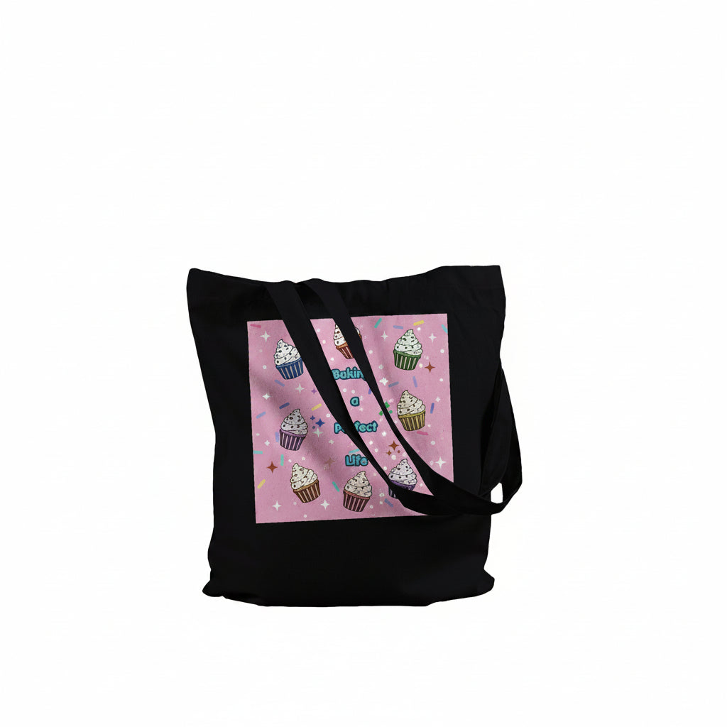 A black canvas tote bag with a square pink graphic print on the front featuring illustrated cupcakes and the text "Baking a perfect Life"