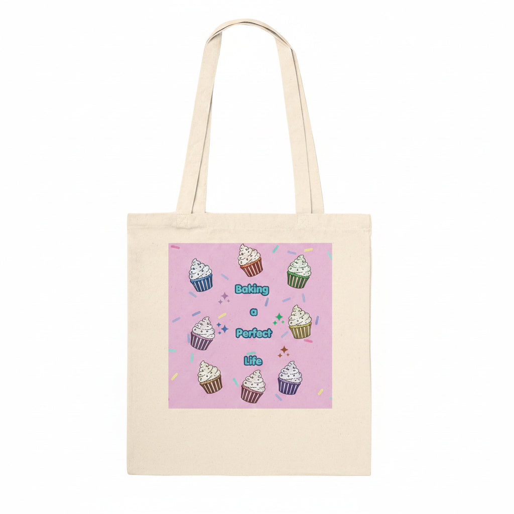 A natural canvas tote bag with a pink square graphic printed on the front, featuring illustrations of cupcakes and the text 'Baking a Perfect life'.