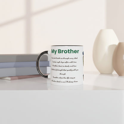 A white ceramic mug with a black handle and rim, printed with a green and black 'My Brother' message, styled on a white surface with books and ceramic vases in the background.