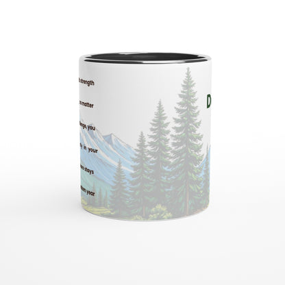 A white ceramic mug with a black interior, featuring a printed graphic of pine trees and mountains with partial text on a white background.