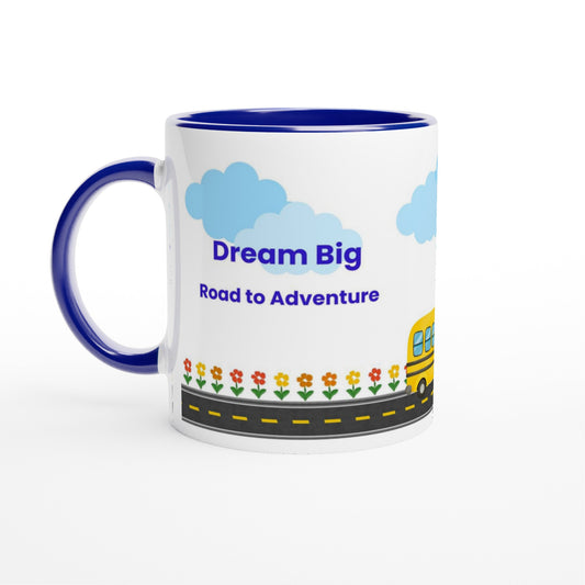 A white ceramic mug with a dark blue handle and interior, featuring a cartoon-style graphic of blue clouds, the text 'Dream Big Road to Adventures,' a yellow school bus, and small flowers along a road.