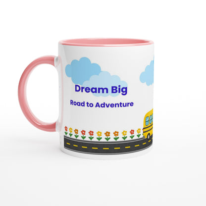 A white ceramic mug with a pink handle and pink interior, printed with the text 'Dream Big Road to Adventures' under blue clouds, a yellow school bus, and a row of colorful flowers along a road.