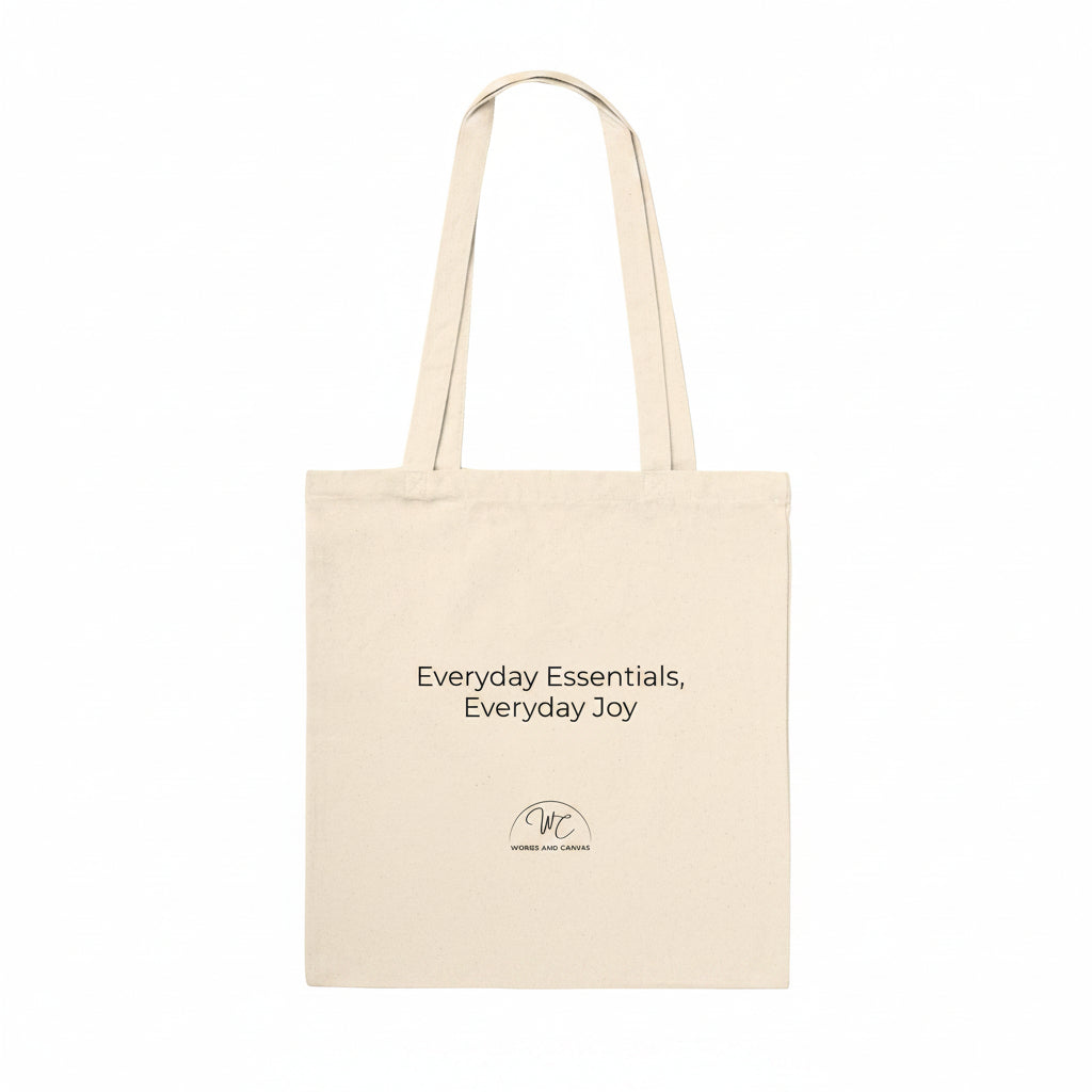 A natural canvas tote bag with black printed text reading 'Everyday Essentials, Everyday Joy' and a small circular logo below, shown on a plain white background.