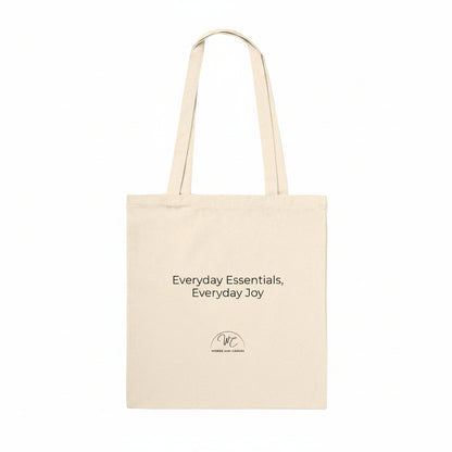 A natural canvas tote bag with black printed text reading 'Everyday Essentials, Everyday Joy' and a small circular logo below, shown on a plain white background.