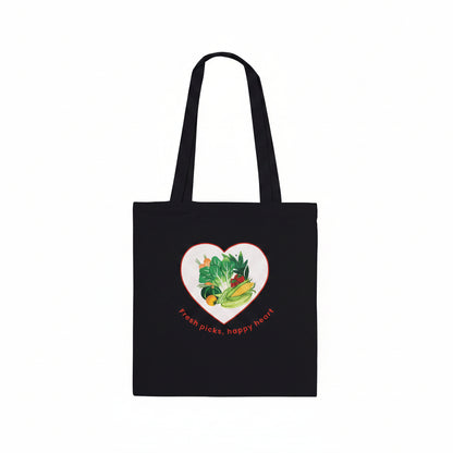 A black canvas tote bag with two shoulder straps, featuring a heart-shaped graphic on the front filled with colorful vegetables and the text 'Fresh picks, happy heart' , shown against a plain white background.