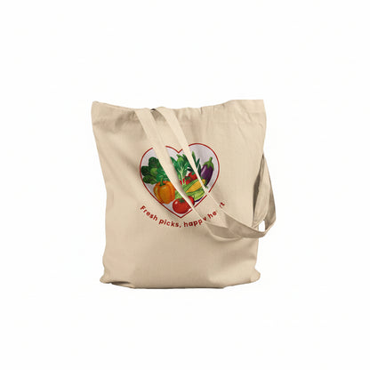 A natural beige canvas tote bag with a colorful heart-shaped vegetable graphic and the text 'fresh picks, happy after' printed on the front, set against a plain white background.