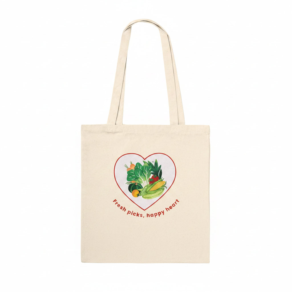 A natural beige canvas tote bag with two shoulder straps, featuring a graphic of various colorful vegetables inside a red heart outline with the text 'Fresh picks, happy heart' printed below.