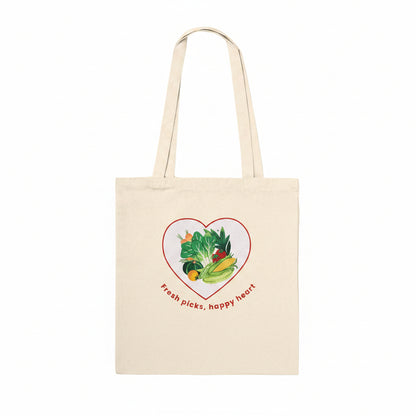 A natural beige canvas tote bag with two shoulder straps, featuring a graphic of various colorful vegetables inside a red heart outline with the text 'Fresh picks, happy heart' printed below.