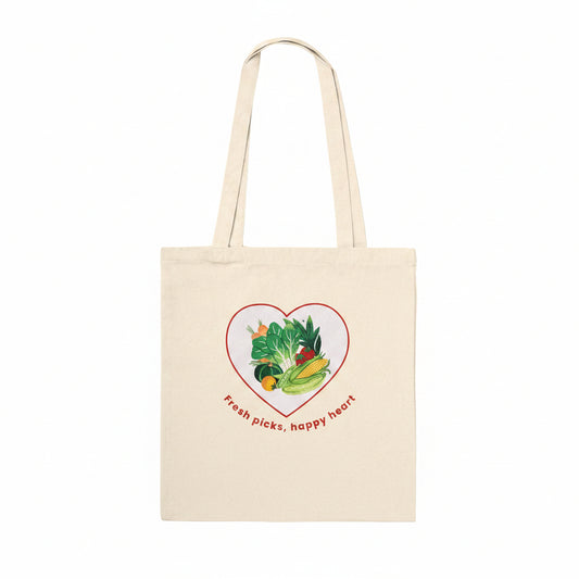 A natural beige canvas tote bag with two shoulder straps, featuring a graphic of various colorful vegetables inside a red heart outline with the text 'Fresh picks, happy heart' printed below.