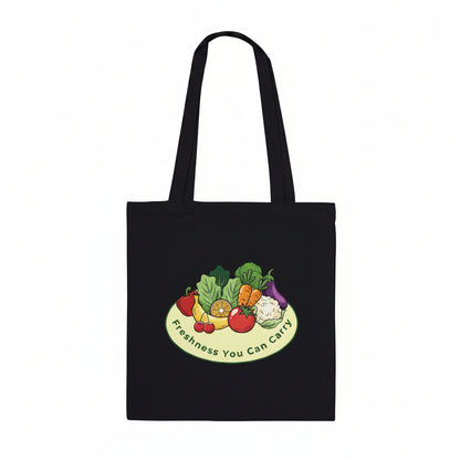A black canvas tote bag with two shoulder straps, featuring a colorful graphic of fresh vegetables on a plate with the text 'Freshness You Can Carry' printed below it, set against a plain white background.