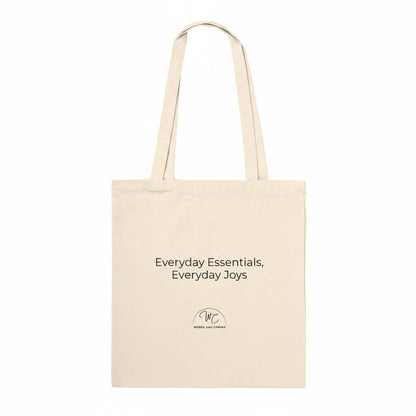 A natural canvas tote bag with black printed text reading 'Everyday Essentials, Everyday Joys' and a small circular 'WC' logo below, shown on a plain white background.