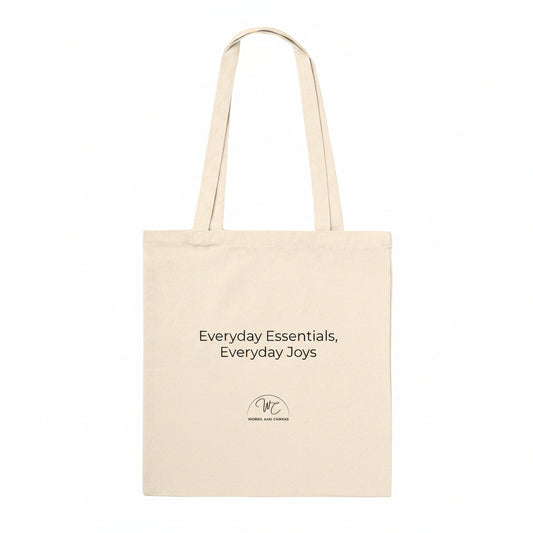 A natural canvas tote bag with black printed text reading 'Everyday Essentials, Everyday Joys' and a small circular 'WC' logo below, shown on a plain white background.