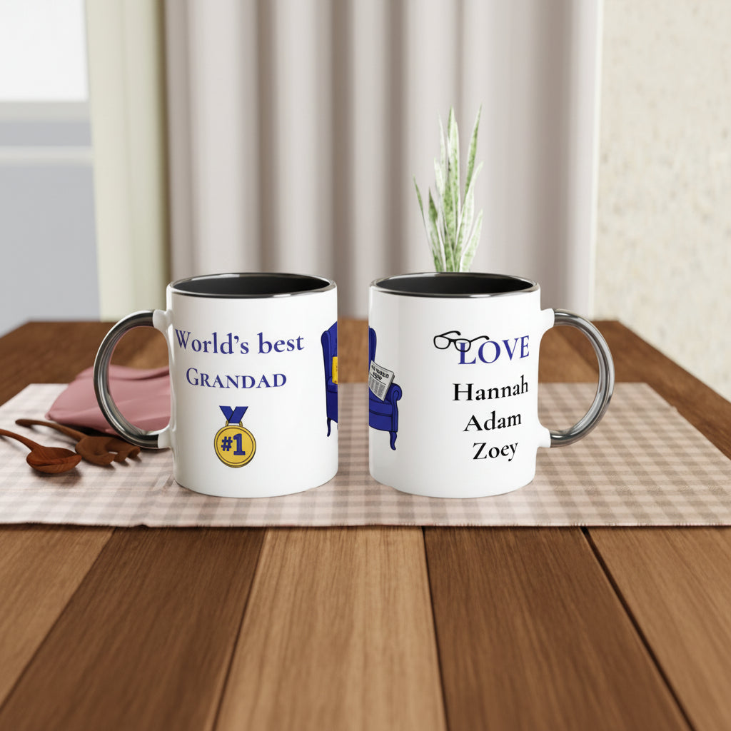Two personalized white ceramic mugs with black interiors and silver-toned handles, displayed on a wooden table. One mug reads 'World's best GRANDAD' with a gold and blue medal graphic, and the other reads 'LOVE Hannah Adam Zoey' with a blue chair graphic.