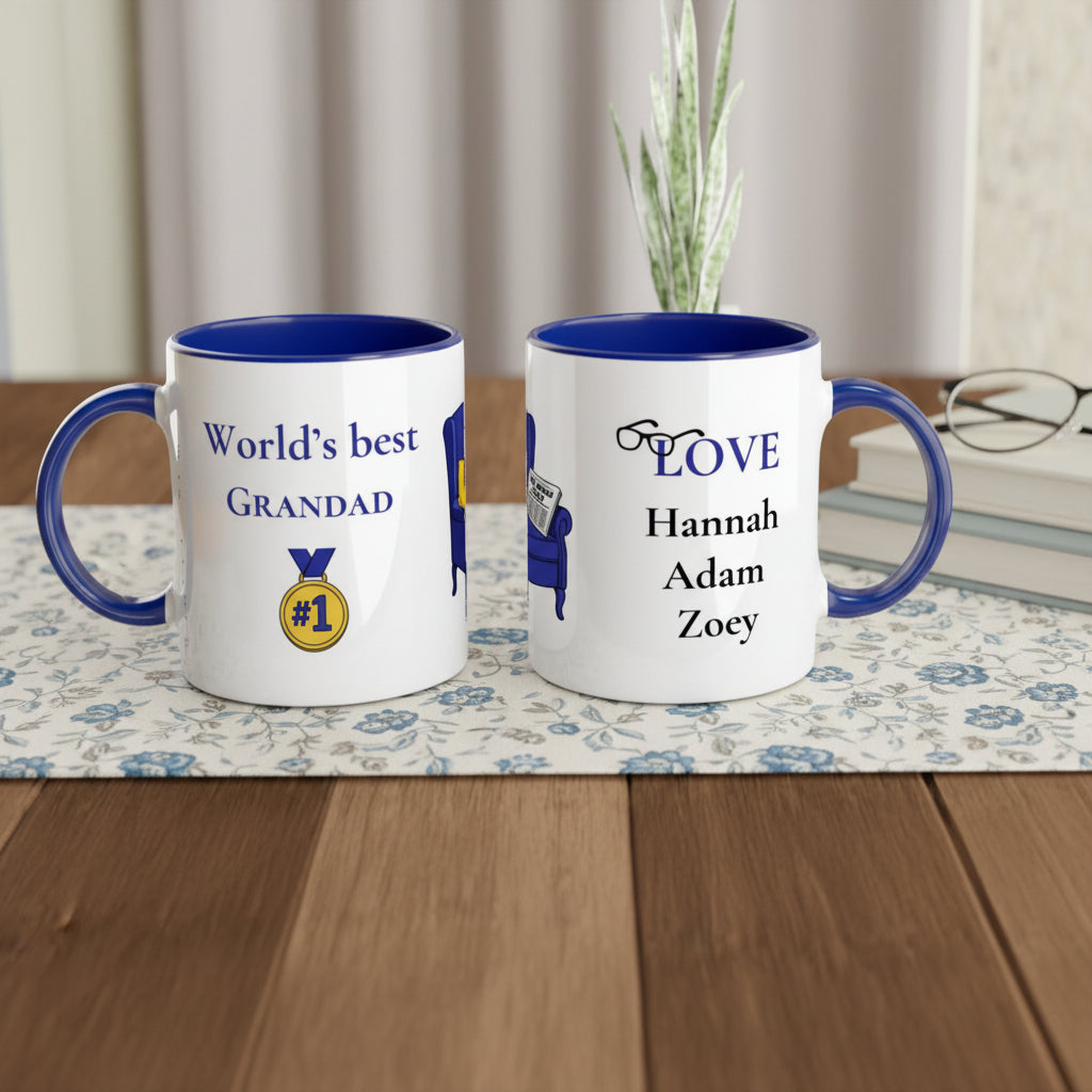 Two personalized white ceramic mugs with blue interiors and handles, displayed side by side on a checkered placemat. The left mug reads 'World's best GRANDAD' with a gold medal graphic, and the right mug reads 'LOVE' above the names 'Hannah', 'Adam', and 'Zoey'.