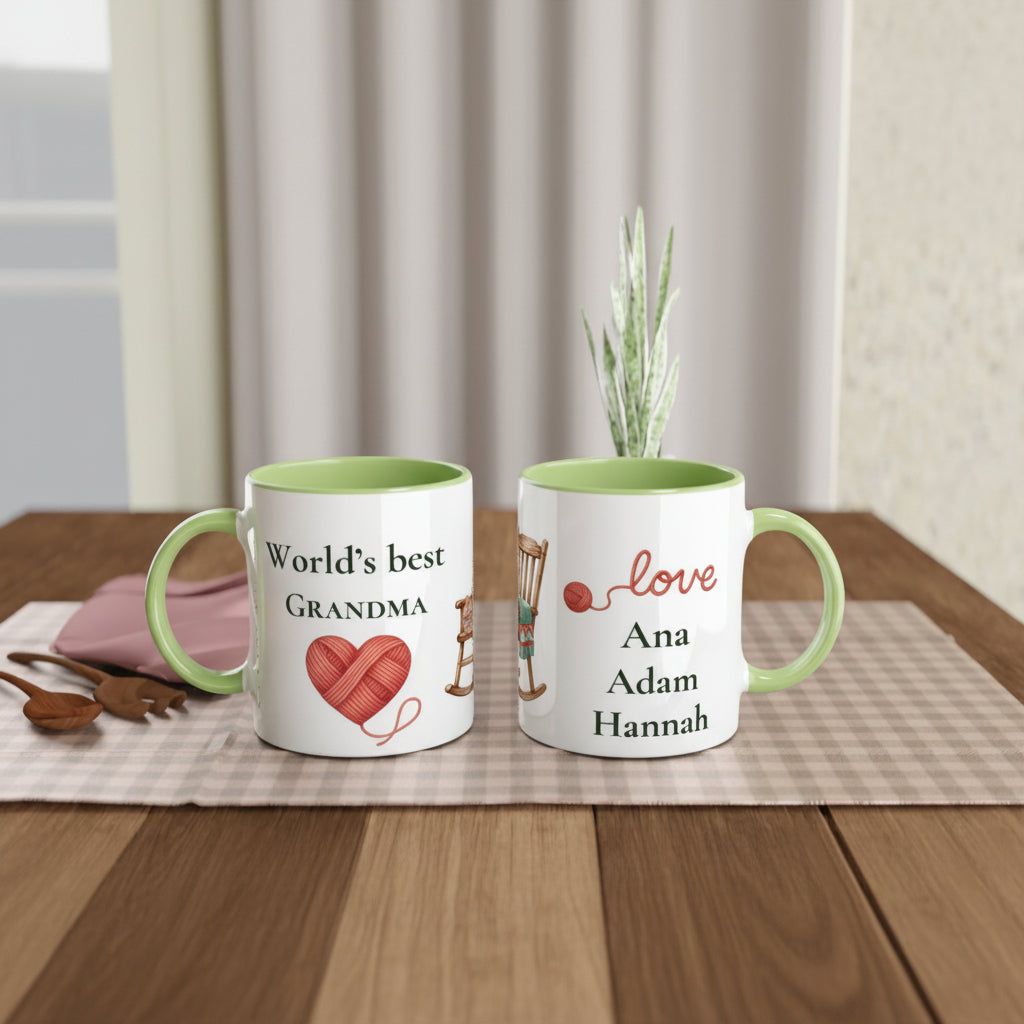 Two personalized ceramic mugs with light green interiors and handles sit on a wooden table. One mug reads 'World's best GRANDMA' with a red heart-shaped yarn ball graphic, and the other reads 'love Ana Adam Hannah' 