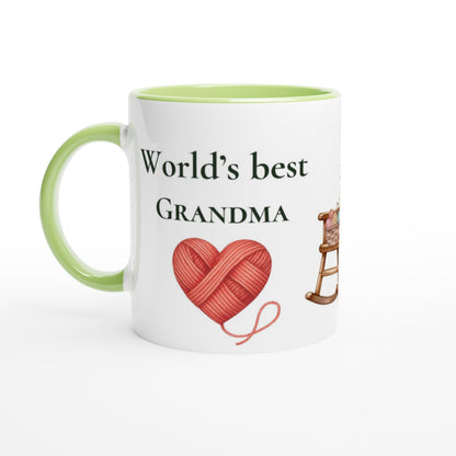 A white ceramic mug with a light green handle and interior, printed with the text 'World's best GRANDMA' above a red heart-shaped yarn ball and a small rocking horse illustration.