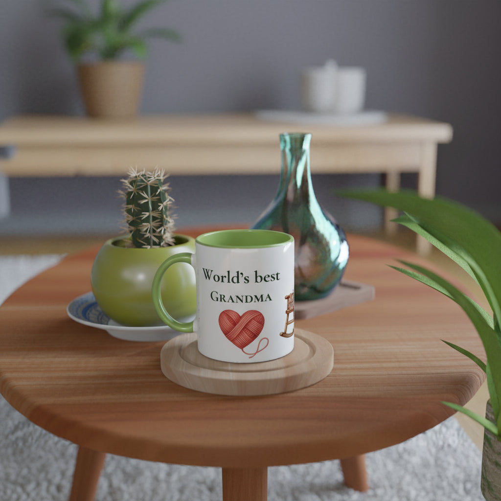 A white ceramic mug with a green interior and handle, printed with the text 'World's best GRANDMA' and a red heart-shaped yarn ball graphic, sitting on a round wooden coaster on a wooden table.