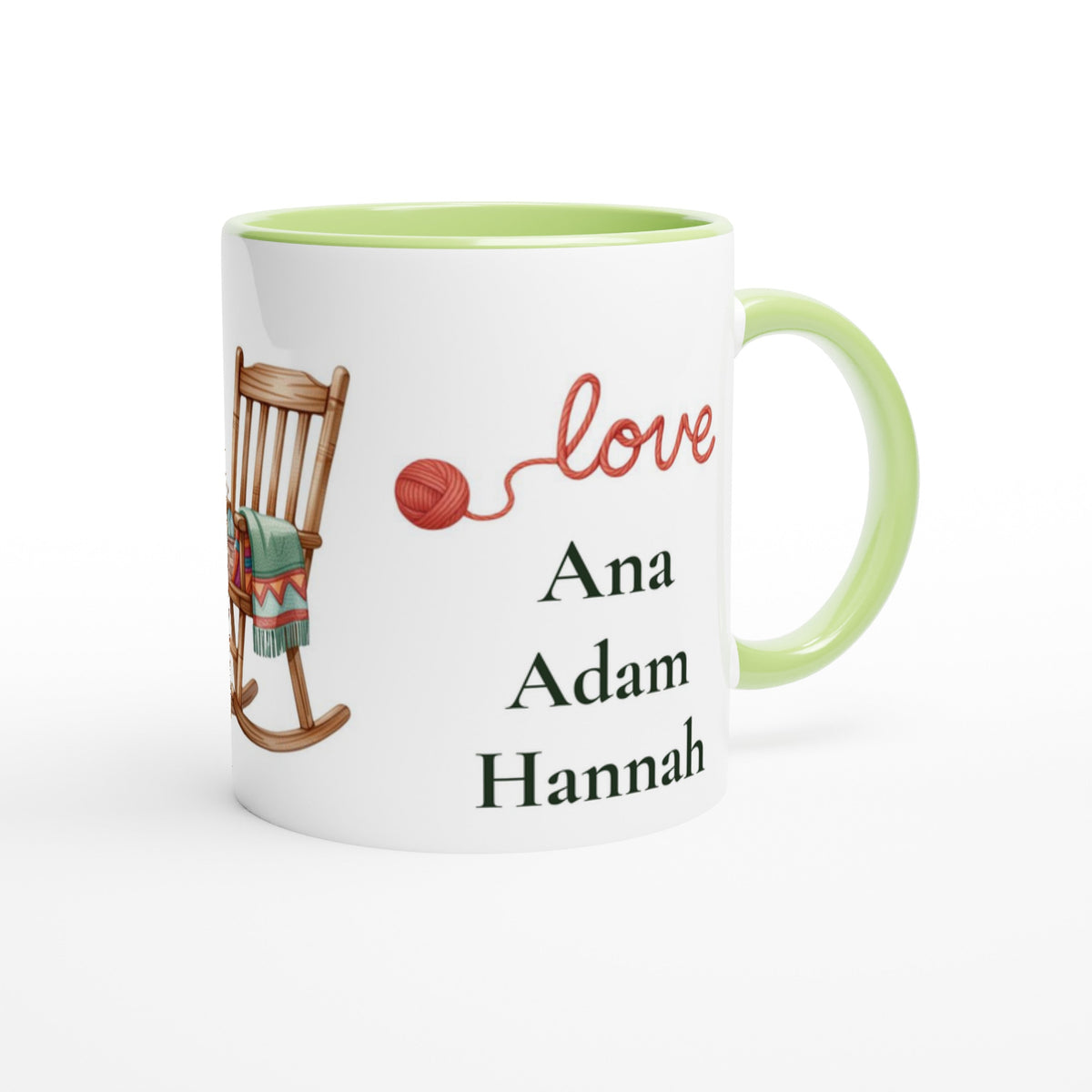A white ceramic mug with a light green handle and interior, featuring a printed design of a wooden rocking chair with a green blanket, a red ball of yarn, the word 'love' in red script, and the names 'Ana', 'Adam', and 'Hannah' 